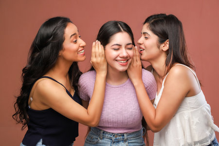 Three young asian women whispering gossip to each other on brown backgroundの写真素材