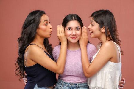 Three young asian women whispering to each other on brown background.の写真素材