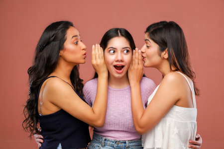 Three young asian women whispering gossip to each other in a studioの写真素材