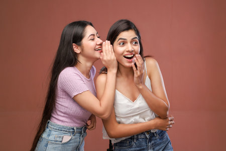 Two young women gossiping and having fun. Studio shot on brown background.の写真素材