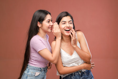 Two young asian women whispering gossip on brown background, copy spaceの写真素材