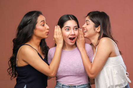 Three young Asian women gossiping with each other on a brown backgroundの写真素材