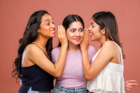Three young asian women whispering to each other on pink background.の写真素材
