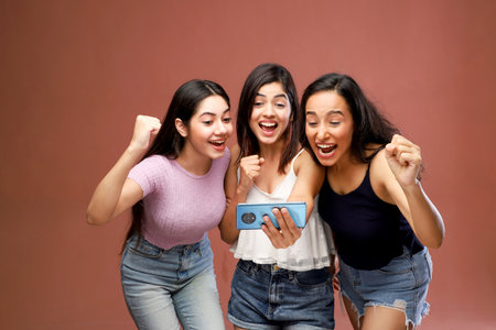 Group of three young asian women using smartphone isolated on brown backgroundの写真素材