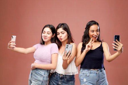 Three young asian women taking selfie with mobile phone on pink backgroundの写真素材