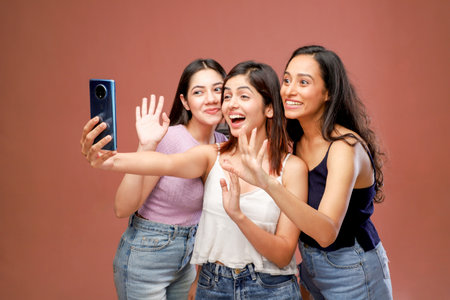 Three asian women taking selfie with mobile phone isolated on brown backgroundの写真素材