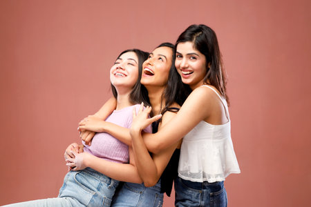 Three young women laughing and hugging each other on a pink background.の写真素材