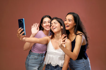 Group of young Asian women taking selfie with mobile phone isolated on brown backgroundの写真素材