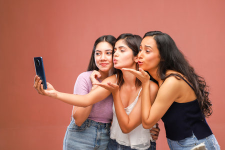 Three young women taking a selfie with a mobile phone and blowing kissesの写真素材