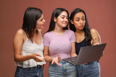 Three young asian women in casual clothes using a laptop computer on a brown backgroundの写真素材