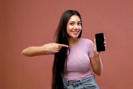 Happy young woman showing smartphone with blank screen and pointing on it.の写真素材