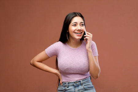 Portrait of a happy young woman talking on mobile phone against brown backgroundの写真素材