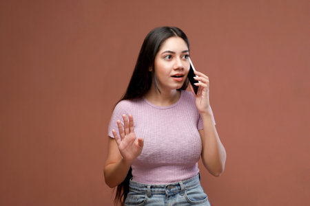 Portrait of a beautiful young woman talking on mobile phone over brown backgroundの写真素材