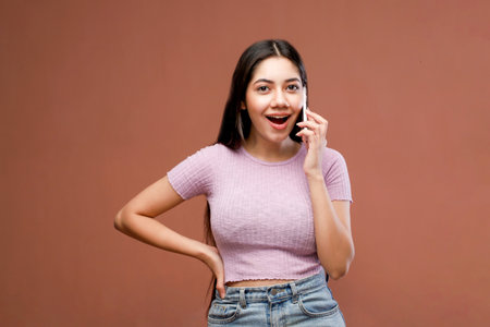 Portrait of a happy young woman talking on mobile phone over brown backgroundの写真素材