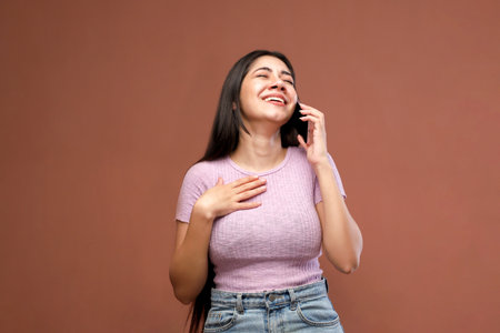 Portrait of a happy young woman talking on the phone over brown backgroundの写真素材