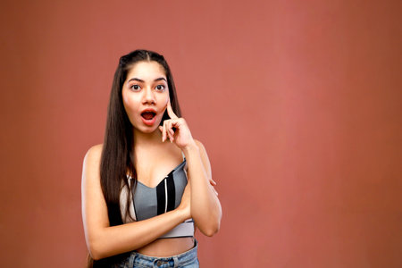 Portrait of a beautiful young woman talking on the phone against brown backgroundの写真素材