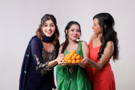 Three women in saree holding sweets and smilingの写真素材
