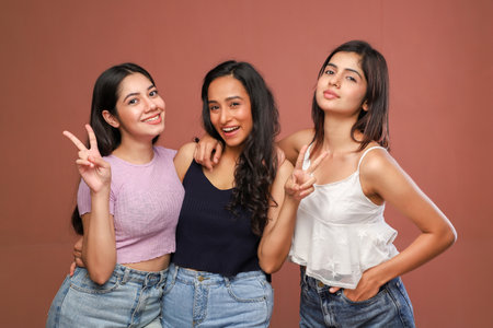 Three happy young women in casual clothes showing victory sign with their fingersの写真素材