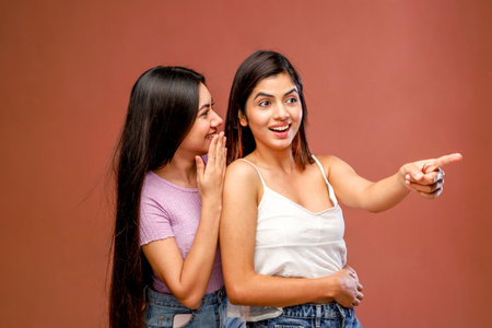 Two young women gossiping and gossiping on a brown background.の写真素材