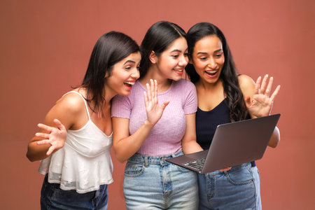 Group of happy young women using laptop computer, isolated on brown backgroundの写真素材