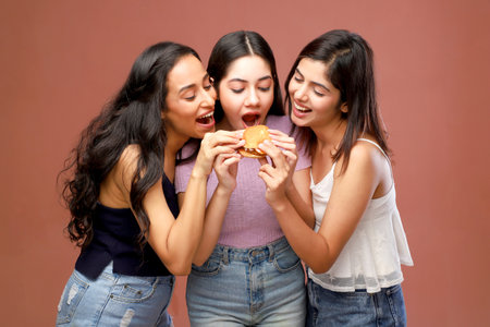 Three beautiful young women eating a hamburger on a brown background.の写真素材