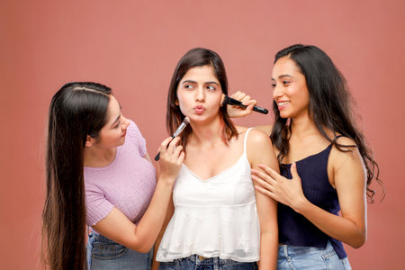 Three beautiful young women applying make up on their faces with a brushの写真素材