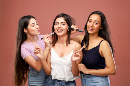 Three young asian women with makeup brushes in their hands isolated on brown backgroundの写真素材