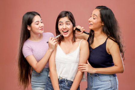 Portrait of three happy young women applying makeup with brush on pink backgroundの写真素材