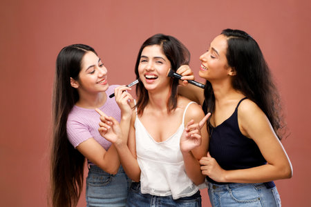 Three beautiful young women applying makeup on their faces on a pink backgroundの写真素材