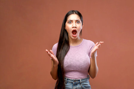Portrait of a surprised young woman looking at camera over brown backgroundの写真素材