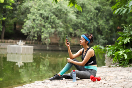 Sporty young woman taking a selfie while sitting on the bank of a lakeの写真素材
