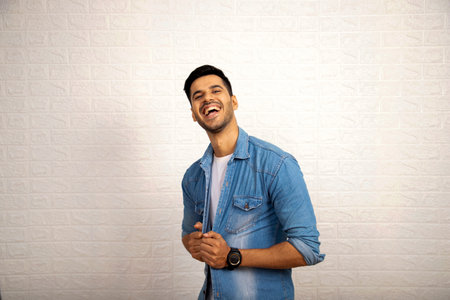Portrait of a young latin man laughing against a white wallの写真素材