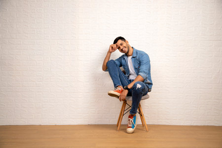 Young Asian man sitting on a chair in a room with a white wallの写真素材