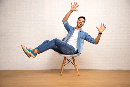 Young man sitting on chair with arms raised and laughing. Indoors.の写真素材