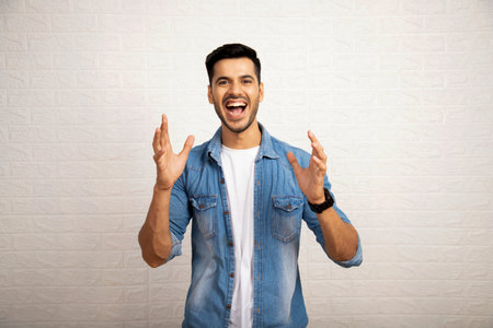Portrait of a happy young man gesturing against white wall backgroundの写真素材