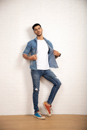 Handsome young man in casual clothes leaning against white wall.の写真素材