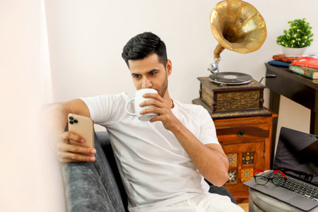 Handsome young man drinking coffee and using smartphone at home.の写真素材