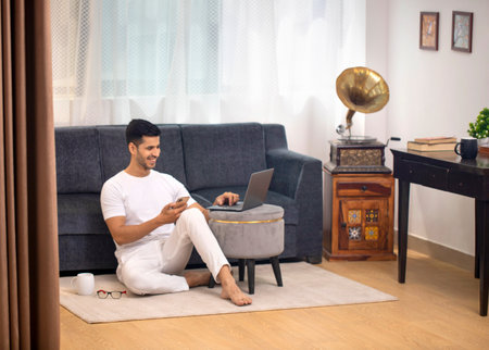 Young man sitting on the floor at home and working on a laptopの写真素材