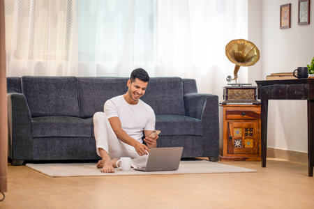 Young man sitting on the floor in front of laptop at home.の写真素材