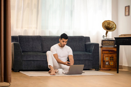 Young Indian man using laptop while sitting on the floor at home.の写真素材