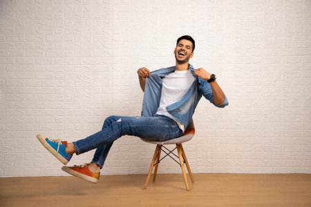 Young man in jeans and a T-shirt sitting on a chair and smilingの写真素材
