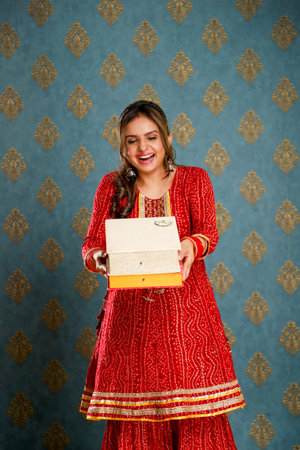 Young indian woman holding a gift box in front of vintage wallpaperの写真素材
