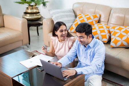 Happy Indian couple using laptop and credit card in living room at homeの写真素材