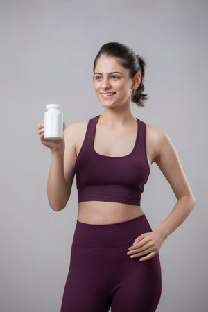 Portrait of a smiling sporty young woman holding a bottle of protein powderの写真素材