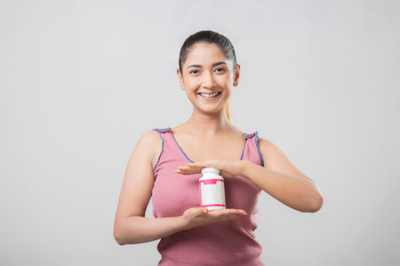 Beautiful asian woman holding a bottle of pills on white backgroundの写真素材