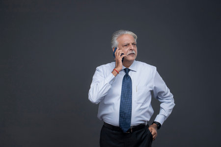 Portrait of senior businessman talking on mobile phone while standing against grey backgroundの写真素材