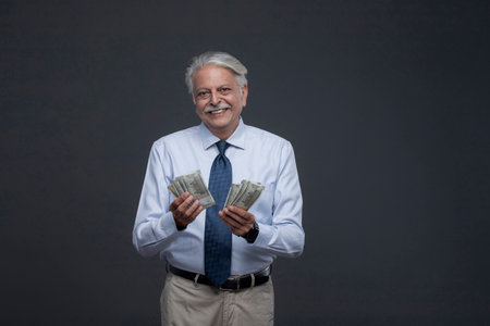 Portrait of a happy senior businessman holding money, isolated on grey backgroundの写真素材