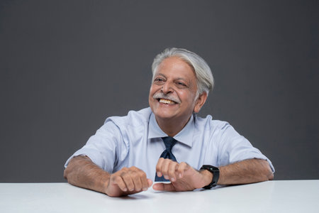 Portrait of happy senior man sitting at table against grey background.の写真素材