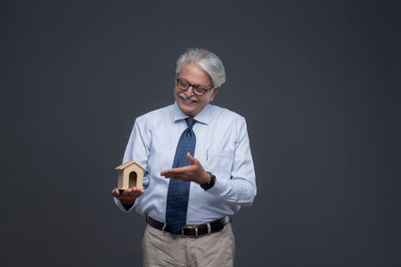 Portrait of senior Asian businessman holding house model over grey background.の写真素材