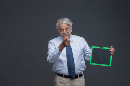Senior asian business man holding a tablet with blank screen on gray backgroundの写真素材